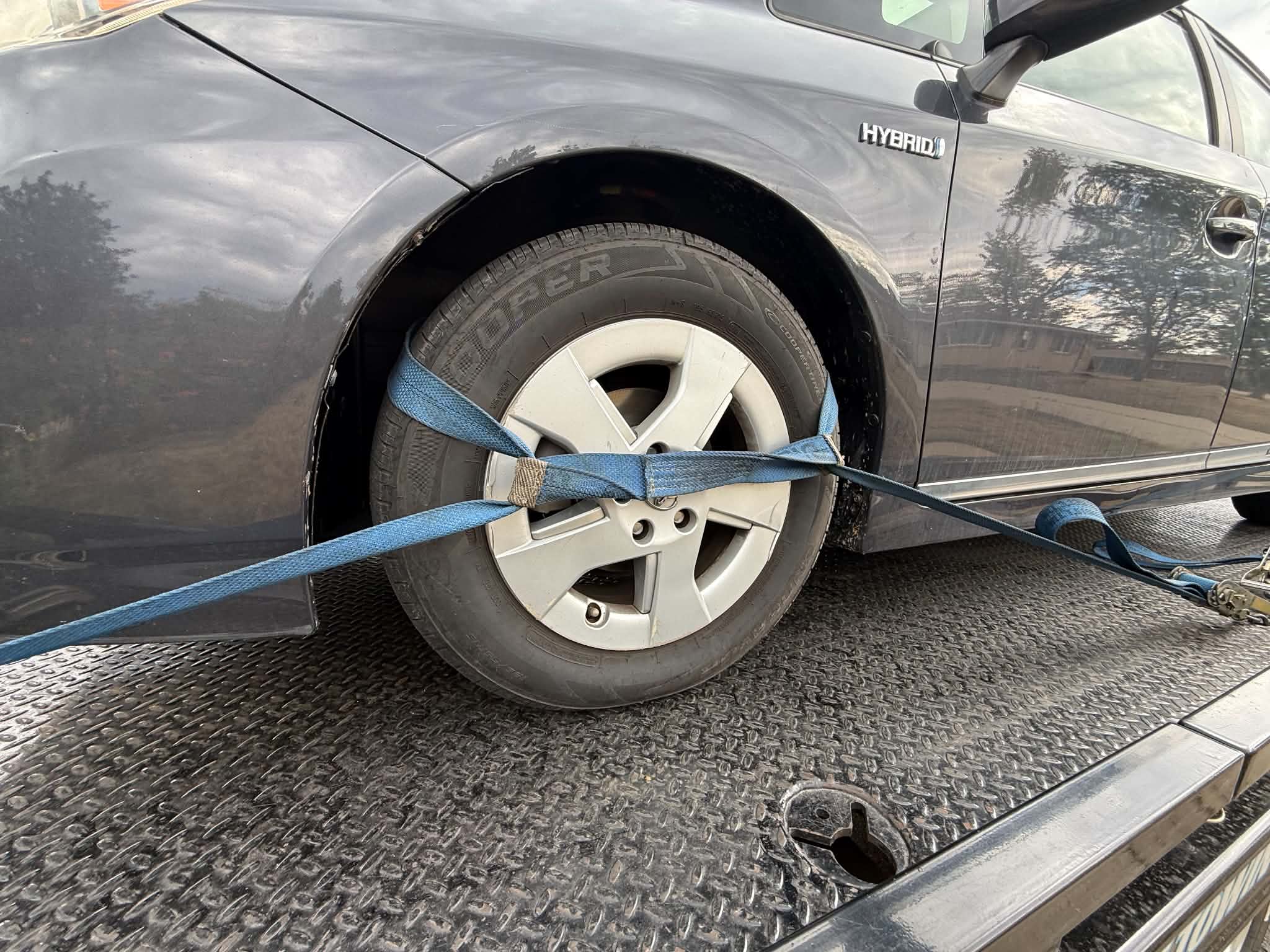 Toyota Prius Hybrid wheel secured on a flatbed with blue straps protecting the plastic wheel cover