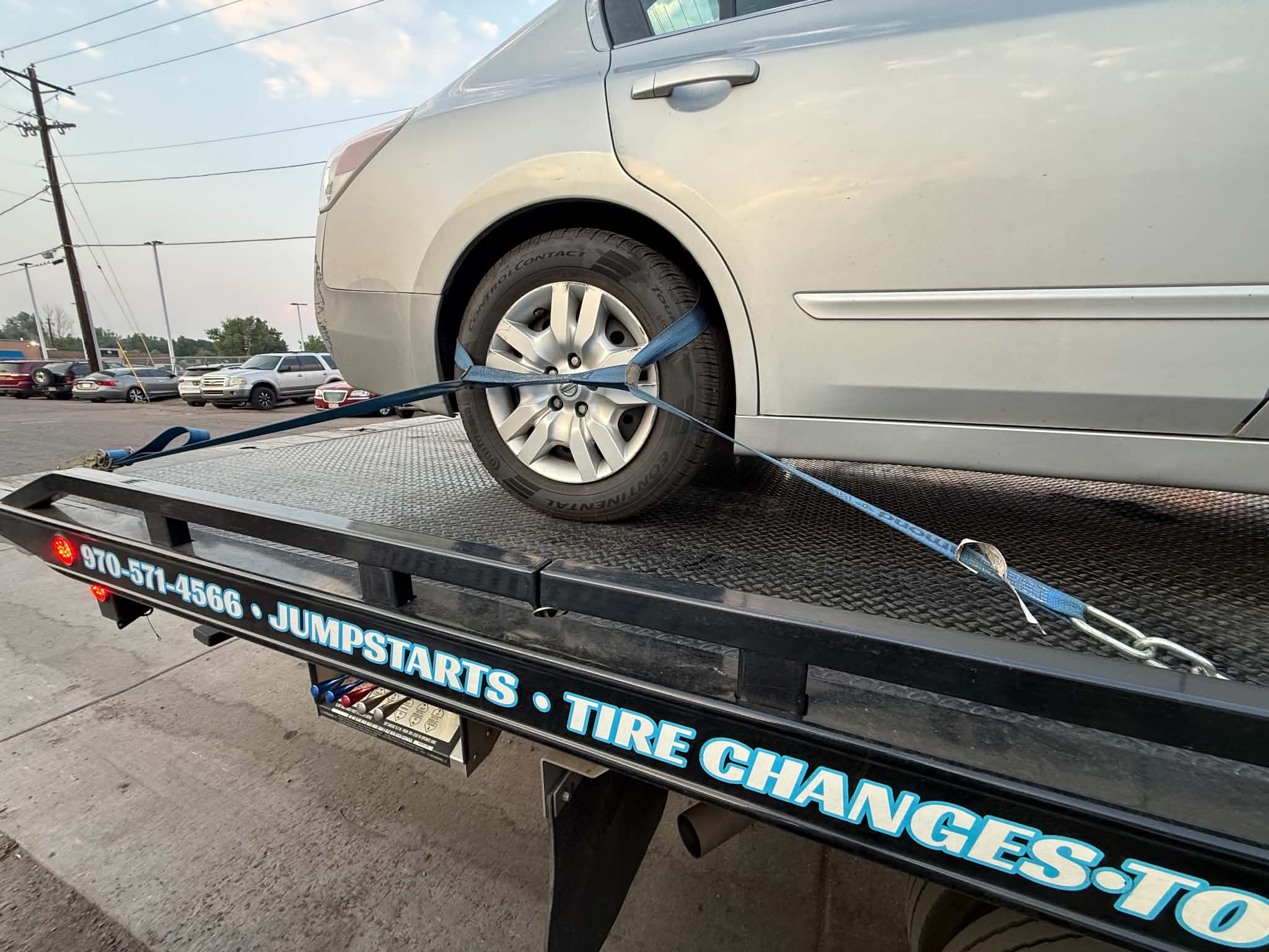 Silver sedan secured on a flatbed with blue tie-down straps