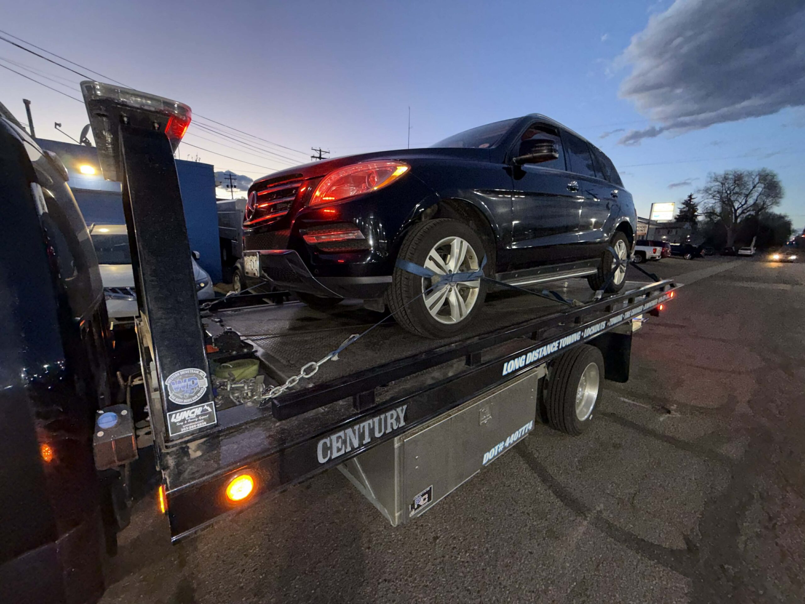 Black SUV secured on a First Response Towing flatbed at dusk