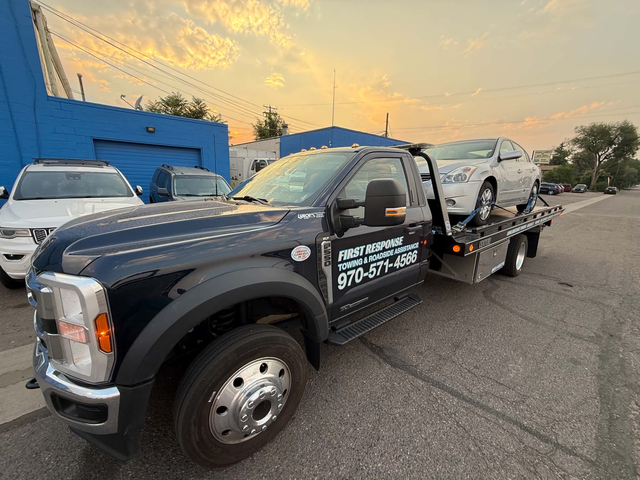 First Response Towing flatbed truck carrying a silver sedan at sunset