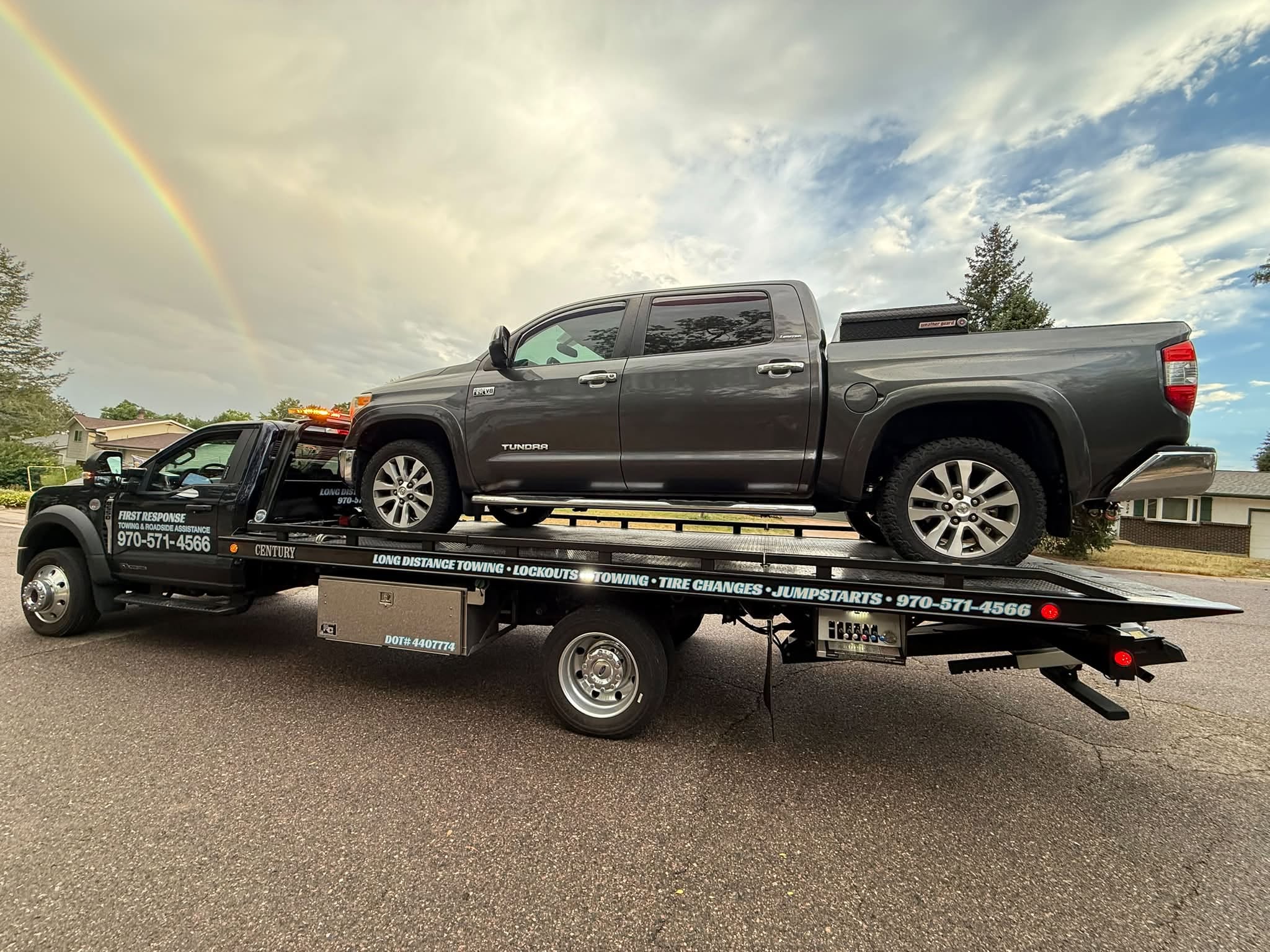Gray Toyota Tundra loaded on a First Response Towing flatbed with a rainbow in the sky