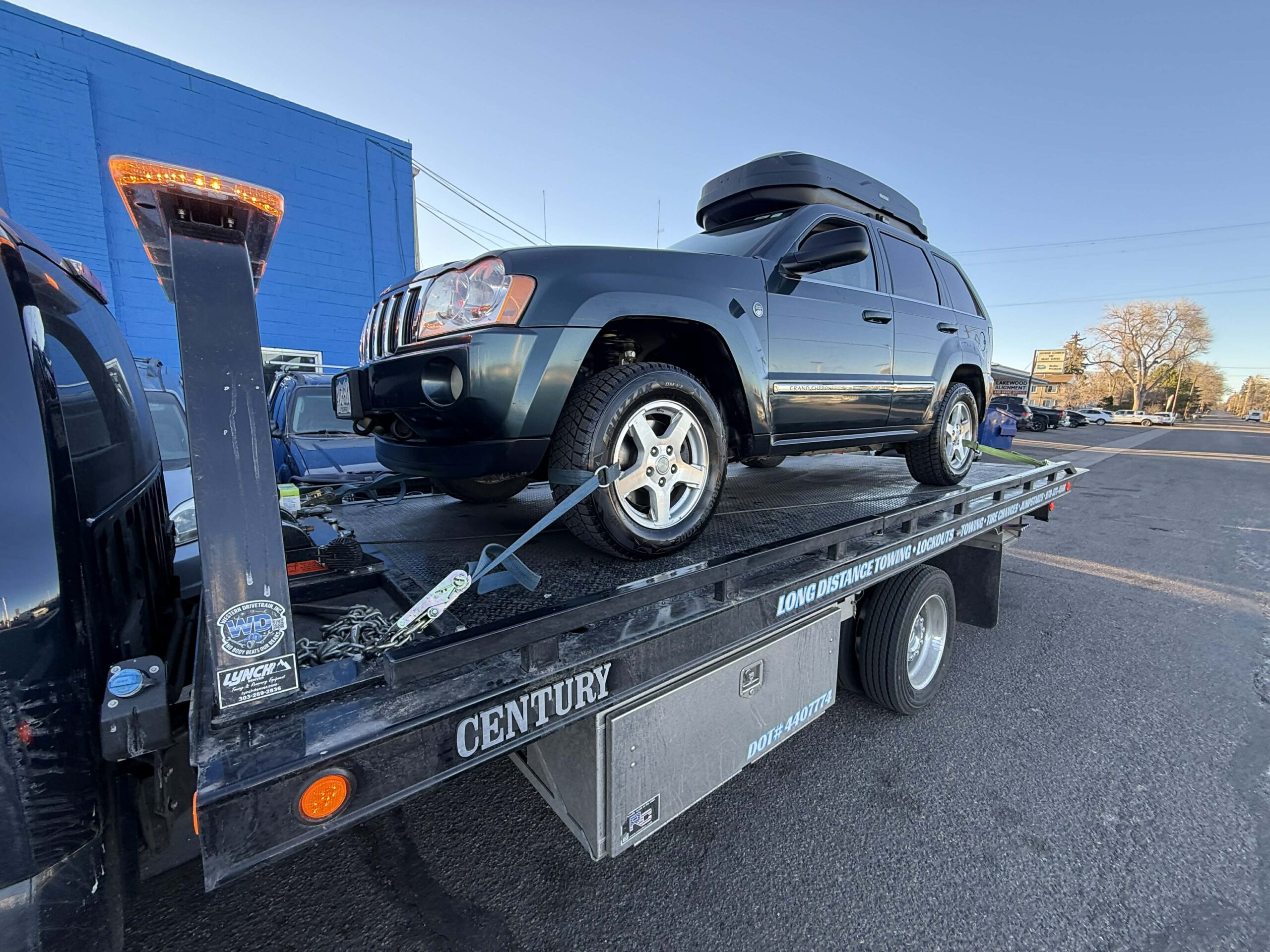 Dark green SUV loaded on a tow truck trailer in front of a blue building